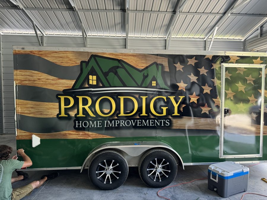 Green 'PRODIGY HOME IMPROVEMENTS' enclosed trailer with American-flag mountain motif on the full side wrap