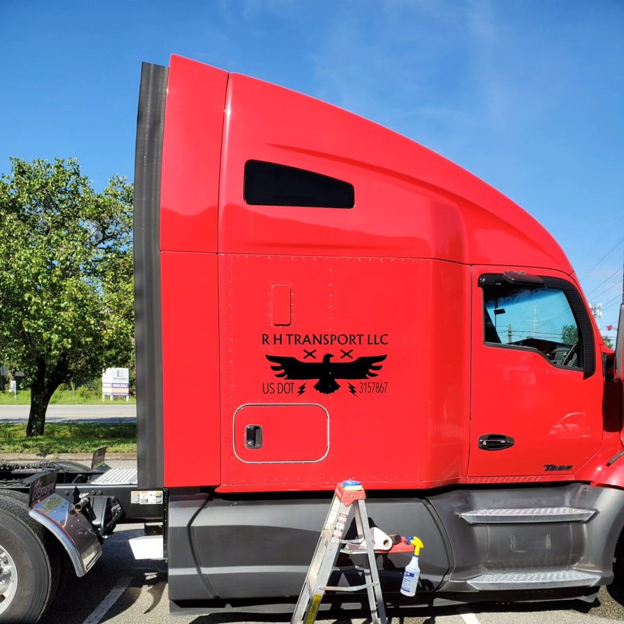Red big-rig cab with 'RH TRANSPORT LLC' door graphics and eagle-mark logo