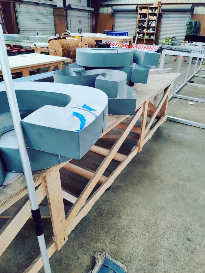 Fresh-primed channel letter shells lined up on a shop cart, Minuteman signs behind, ready for face installation