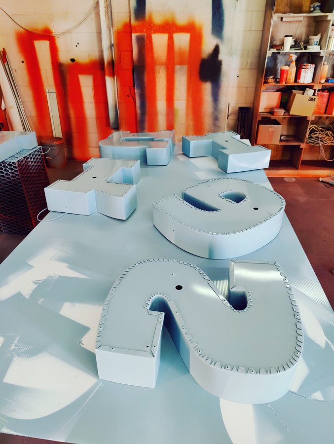 Grey-primed channel letters on a shop table with spray-tested wall behind, ready for finish paint