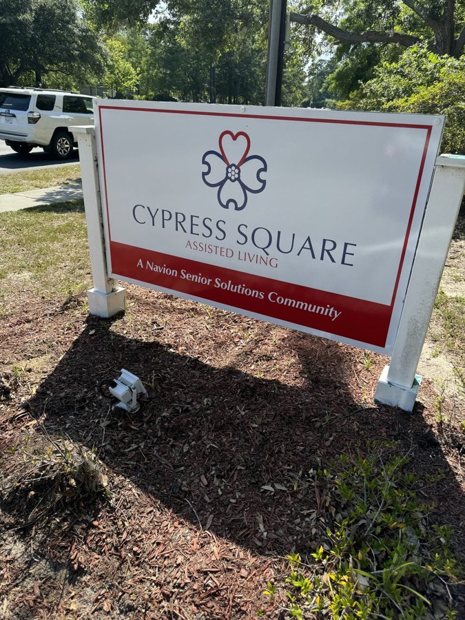 White 'CYPRESS SQUARE' community monument sign on white posts in a mulched bed