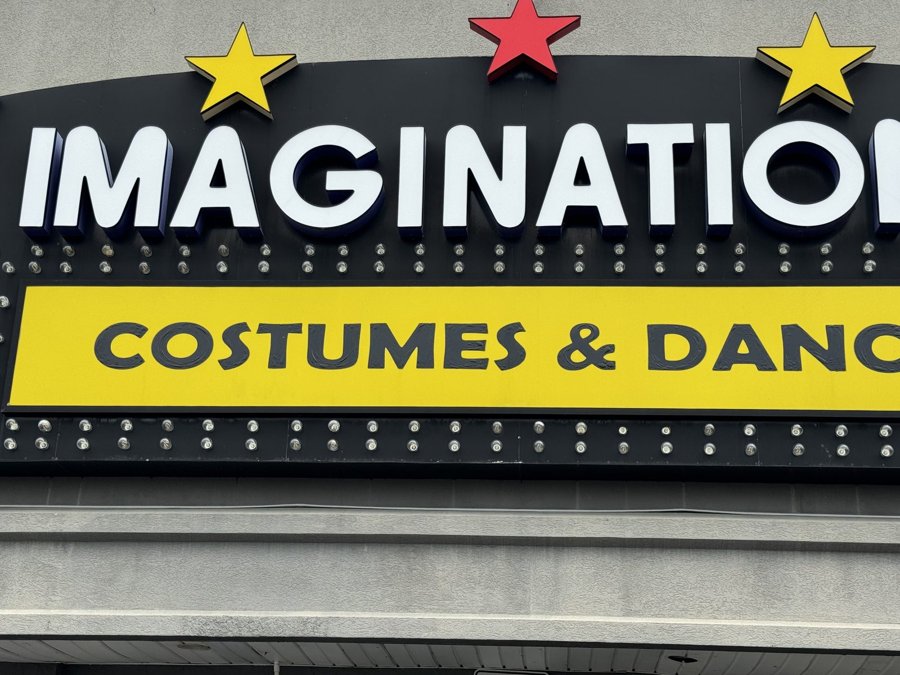 Illuminated 'IMAGINATION COSTUMES & DANCE' storefront channel letters with a row of red and yellow stars above