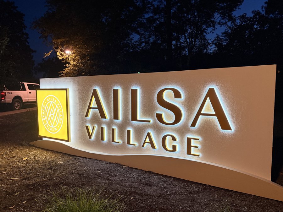 Ailsa Village monument sign illuminated at night with halo-lit letters