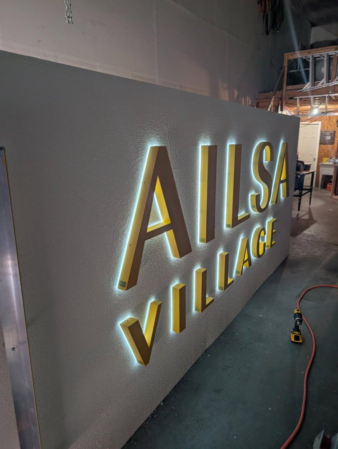 Illuminated AILSA VILLAGE dimensional letters mounted on a wall inside the leasing office