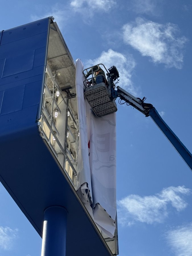 Boom lift positioned high against a metal building for exterior sign work