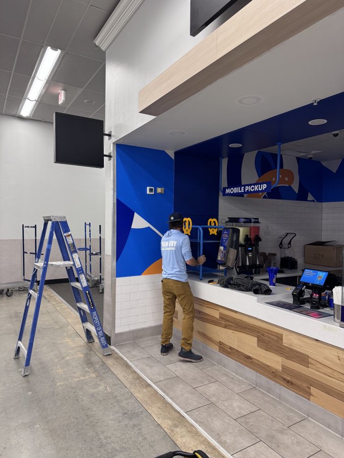 Worker on ladder installing blue wall treatment in slushie bar