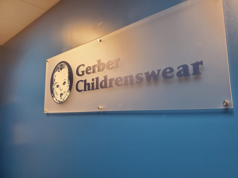 Brushed-metal 'Gerber Childrenswear' dimensional panel sign mounted on a blue-gray interior wall